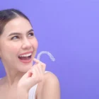 Woman holding a clear retainer while smiling - VanderWall Orthodontics