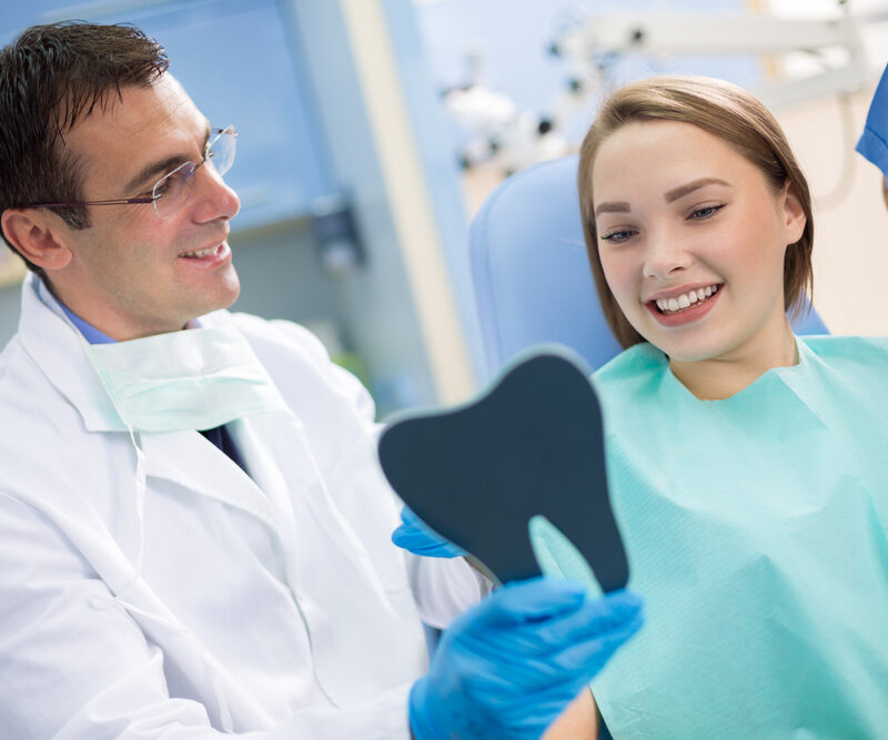 An orthodontist reviewing a patient’s smile using a handheld mirror during a modern orthodontic consultation in a Raleigh clinic.