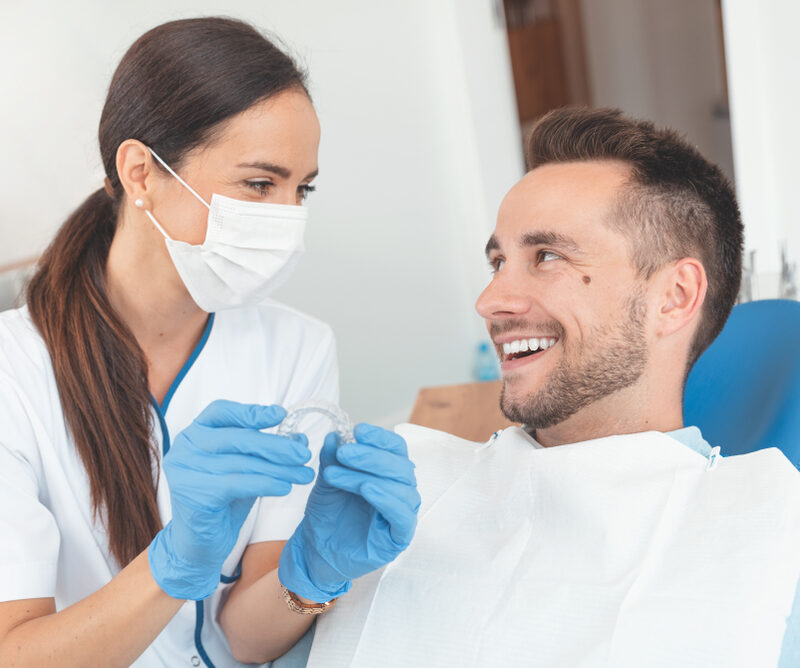 An orthodontic professional explaining clear aligners to a first-time adult patient during an initial consultation in a Triangle Area office.